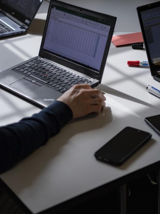 Ein Schreibtisch mit aufgeklappten Laptops, Smartphones und Stifte liegen herum.