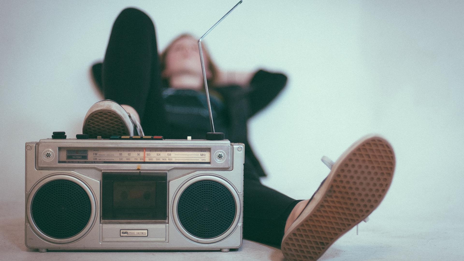 Eine Frau liegt mit einem angewinkelten Bein auf dem Boden, vor ihr steht ein altes Radiogerät.