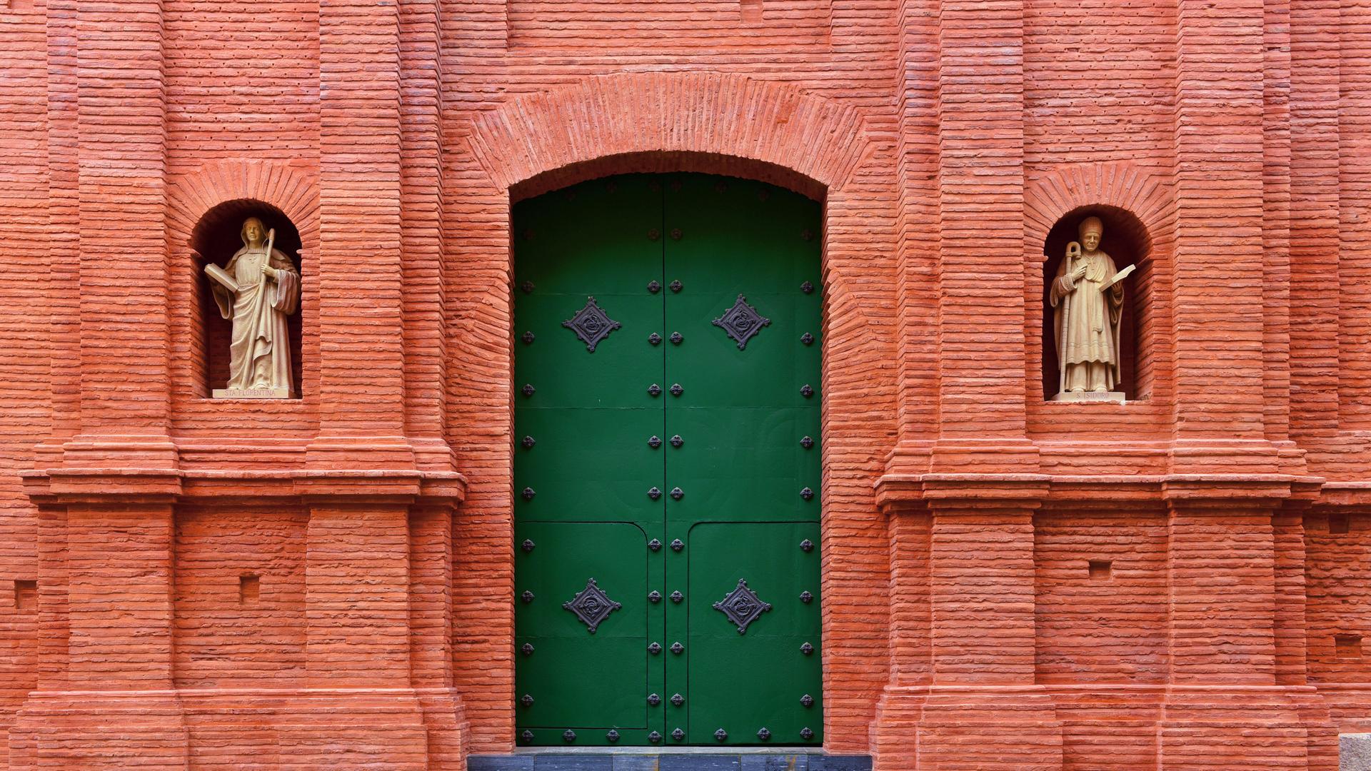 Außenansicht der Kathedrale von Cartagena mit rotem Tor, grüner Tür uns zwei Heiligenfiguren (Symbolbild)