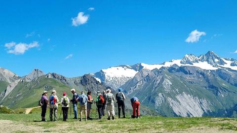 Eine Gruppe Wandertouristen steht vor dem Massiv des Großglockners im Nationalpark Hohe Tauern.
