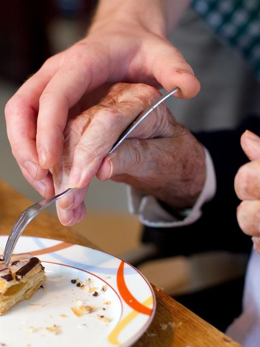Ein junger Mann hilft einer Bewohnerin einer Alzheimer-Wohngemeinschaft beim Einnehmen einer Mahlzeit. 