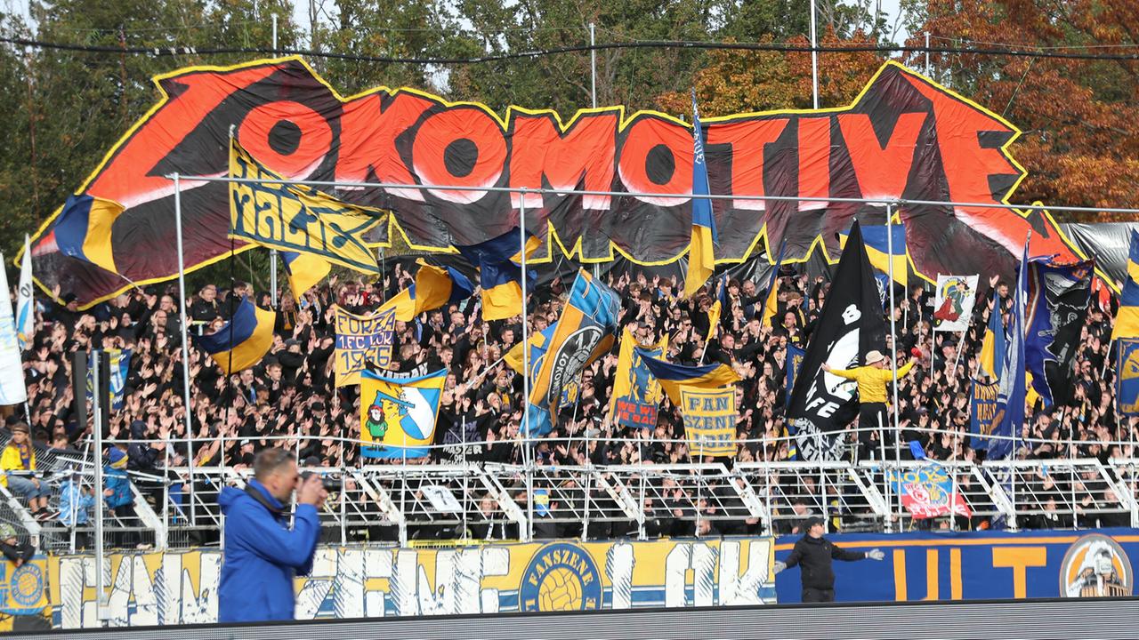 Blick auf den Lok-Leipzig-Fanblock beim Regionalliga-Spiel gegen BSG Chemie Leipzig. Die Fans halten Fahnen in die Luft und ein großes Banner mit der Aufschrift "Lokomotive".