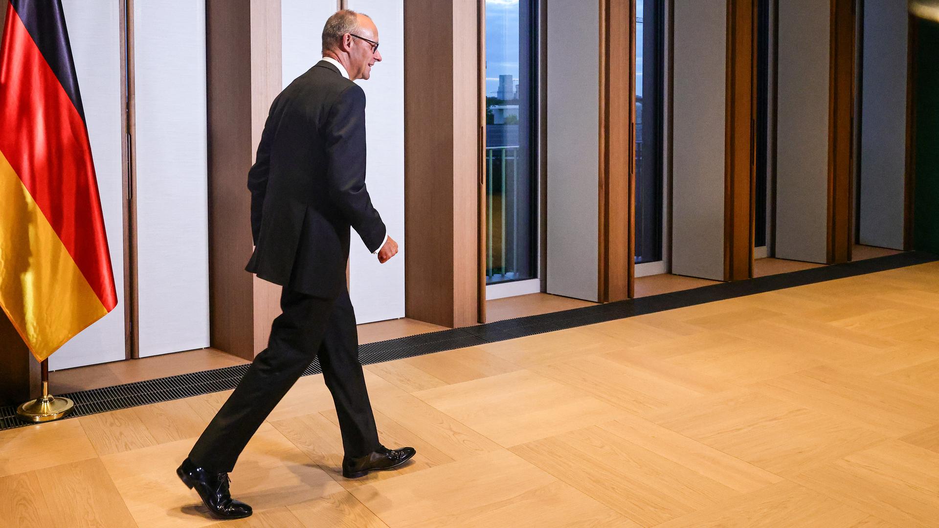 Bundeskanzler Merz geht durch einen Flur, neben ihm die deutsche Flagge.