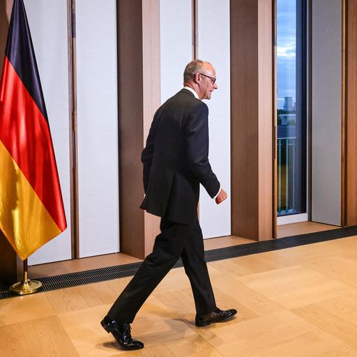Der deutsche Bundeskanzler Friedrich Merz trifft am 10. September 2026 zu einem Galadinner in der offiziellen Residenz des Bundespräsidenten am Spreebogen in Berlin ein. Er geht durch einen Flur, neben ihm die deutsche Flagge.