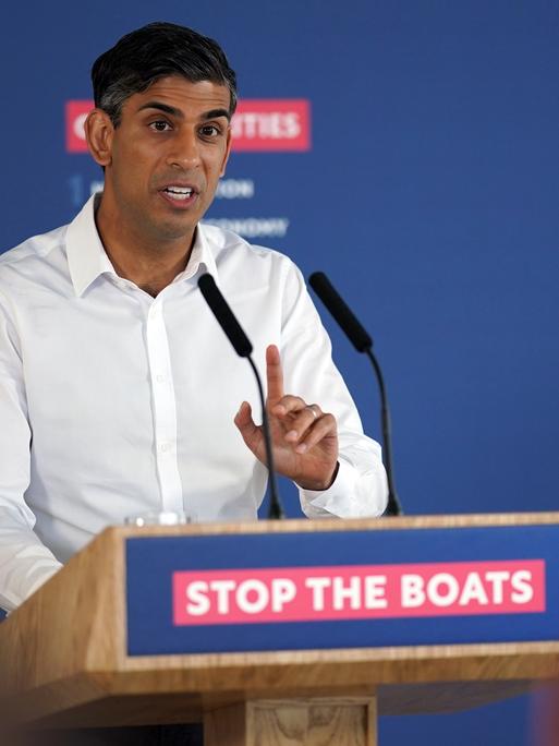 Rishi Sunak spricht während einer Pressekonferenz. An seinem Podium ist der Slogan "Stop the Boats" angebracht.