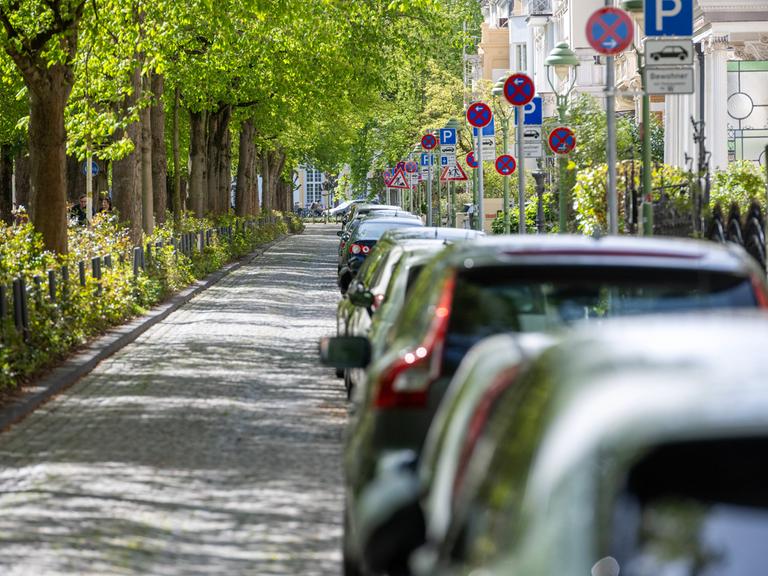 Schilderwald auf der Poppelsdorfer Allee in Bonn. Am Straßenrand parkt ein Auto nach dem anderen. Halteverbotsschilder sollen die Parkplätze für die Autos der Anwohnenden reservieren. 