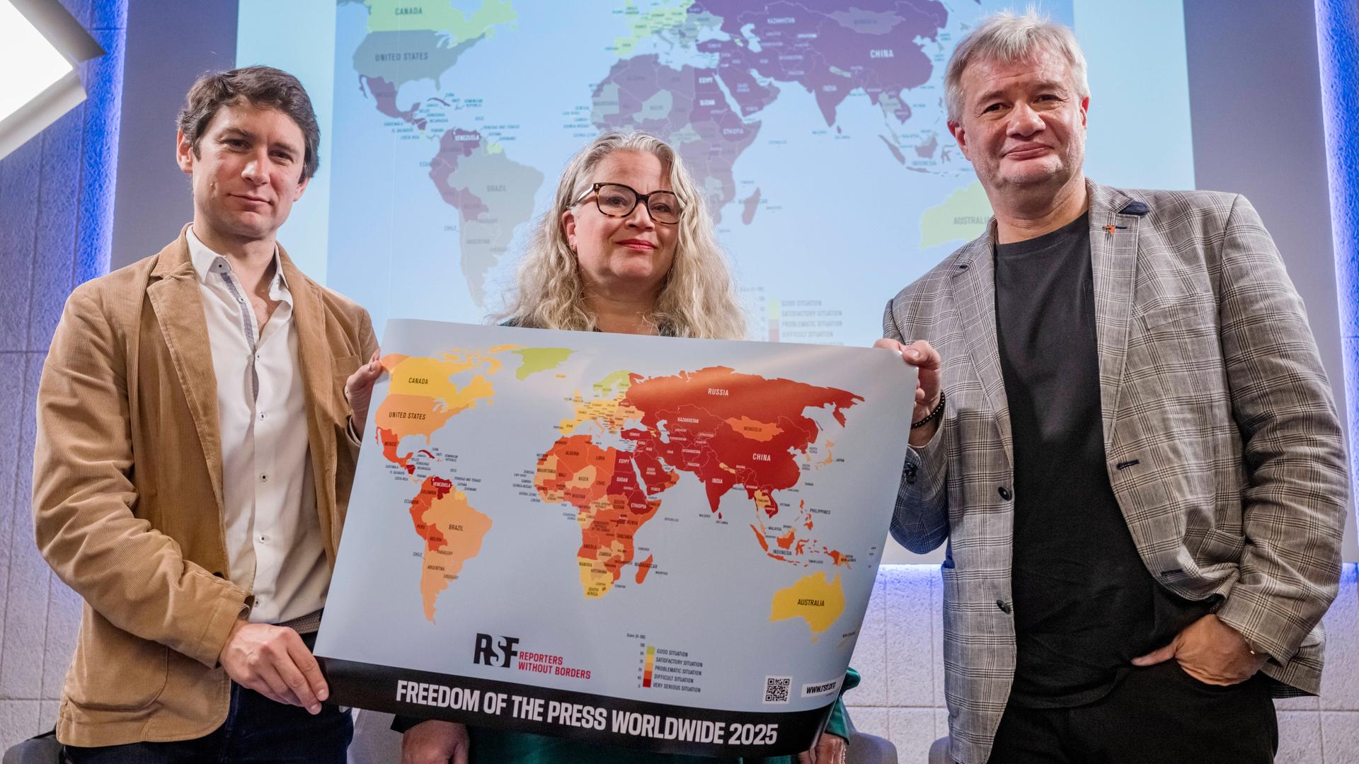 Pavol Szalai (li) von Reporter ohne Grenzen und Journalisten-Kollegen halten bei der Vorstellung des neuen World Press Freedom Index 2025 eine Weltkarte, die die Sicherheit für Journalistinnen und Journalisten weltweit dokumentiert. 