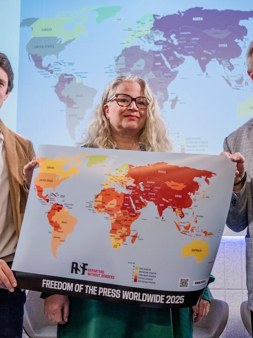 Pavol Szalai (li) von Reporter ohne Grenzen und Journalisten-Kollegen halten bei der Vorstellung des neuen World Press Freedom Index 2025 eine Weltkarte, die die Sicherheit für Journalistinnen und Journalisten weltweit dokumentiert. 