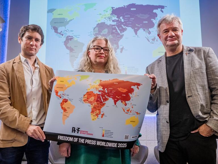 Pavol Szalai (li) von Reporter ohne Grenzen und Journalisten-Kollegen halten bei der Vorstellung des neuen World Press Freedom Index 2025 eine Weltkarte, die die Sicherheit für Journalistinnen und Journalisten weltweit dokumentiert. 