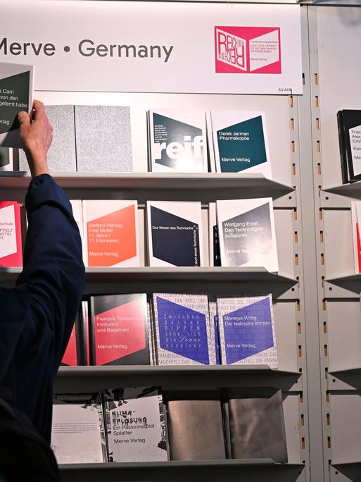 Eine Frau greift nach einem Buch, das in einem Regal des Merve Verlags auf der Frankfurter Buchmesse steht. 