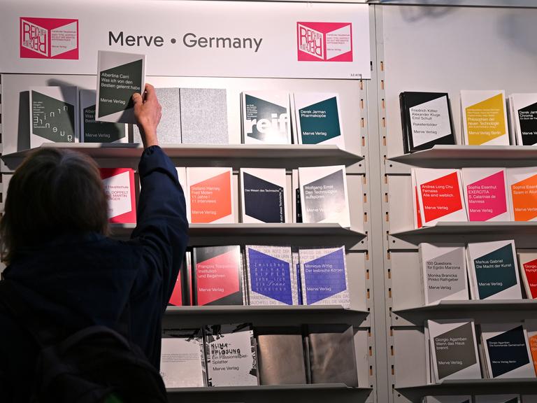 Eine Frau greift nach einem Buch, das in einem Regal des Merve Verlags auf der Frankfurter Buchmesse steht. 