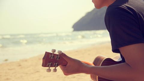 Blick von hinten auf einen Menschen, der am Meer Ukulele spielt.