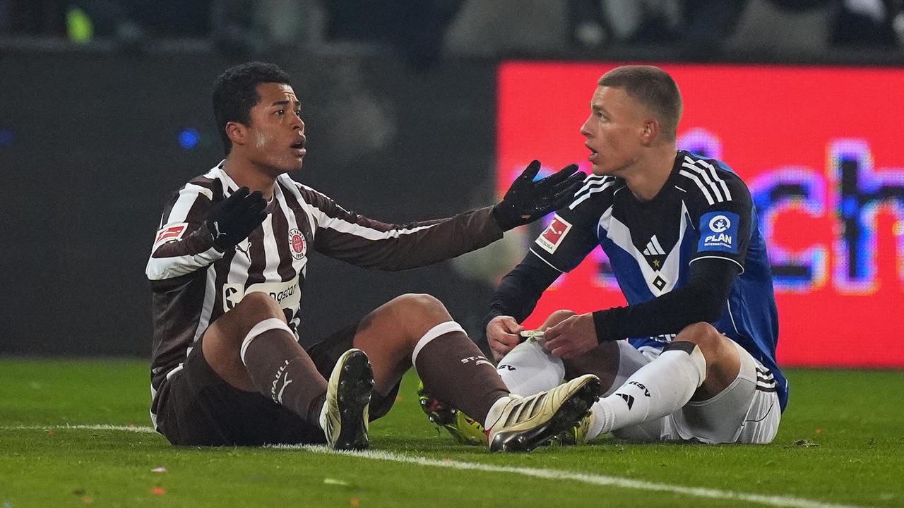 Joel Chima Fujita (l., FC St. Pauli) und Miro Muheim (Hamburger SV) sitzen auf dem Rasen und diskutieren.