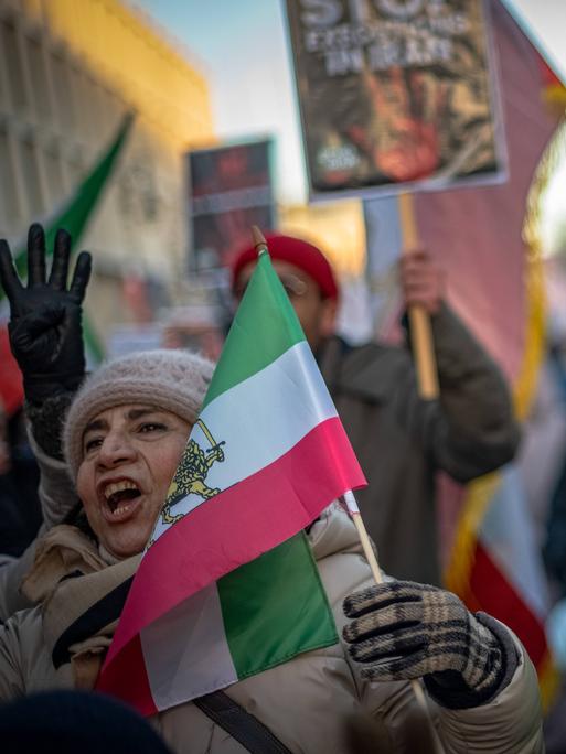 Zwei Frauen demonstrieren zusammen mit anderen Menschen. Sie tragen iranische Flaggen, rufen und heben dabei die Hände. Zwei Frauen demonstrieren zusammen mit anderen Menschen. Sie tragen iranische Flaggen, rufen und heben dabei die Hände.