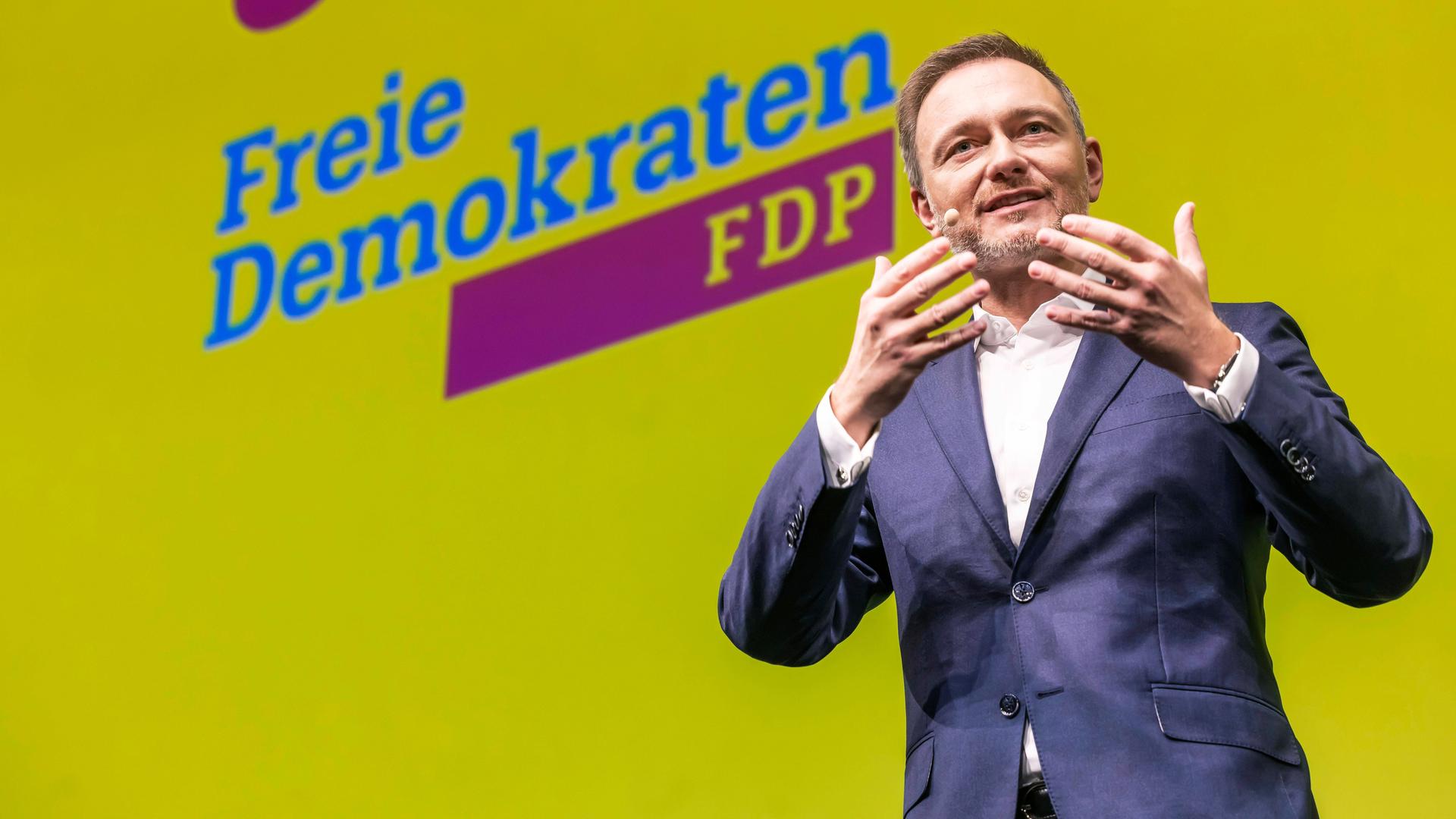 Christian Lindner steht vor einem gelben FDP-Plakat und gestikuliert