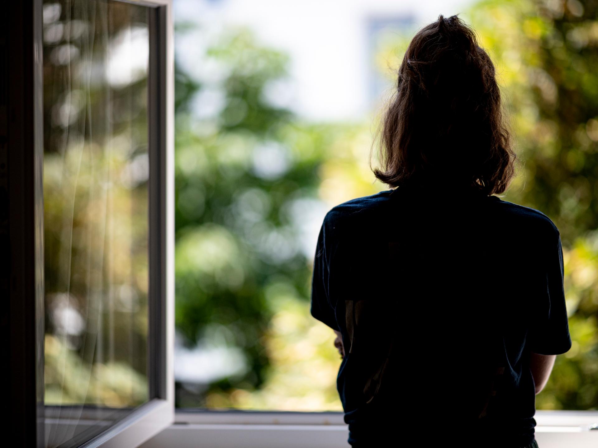 Eine Frau steht in ihrer Wohnung an einem Fenster.