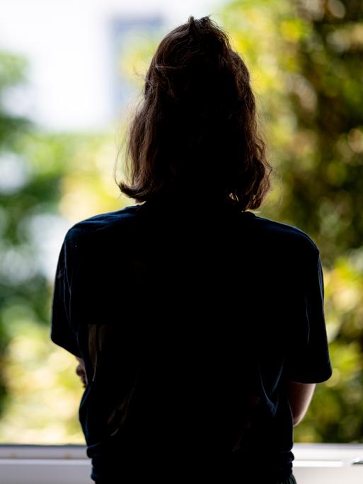 Eine Frau steht in ihrer Wohnung an einem Fenster.