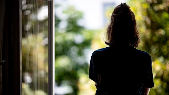 Eine Frau steht in ihrer Wohnung an einem Fenster.