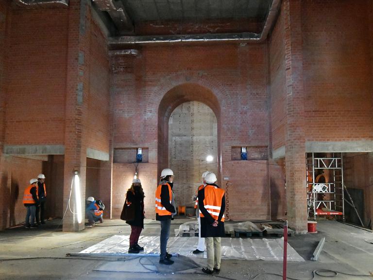 Mehrere Personen mit Bauhelmen besichtigen die noch im Rohbau befindliche Kapelle der Garnisonskirche in Potsdam. 