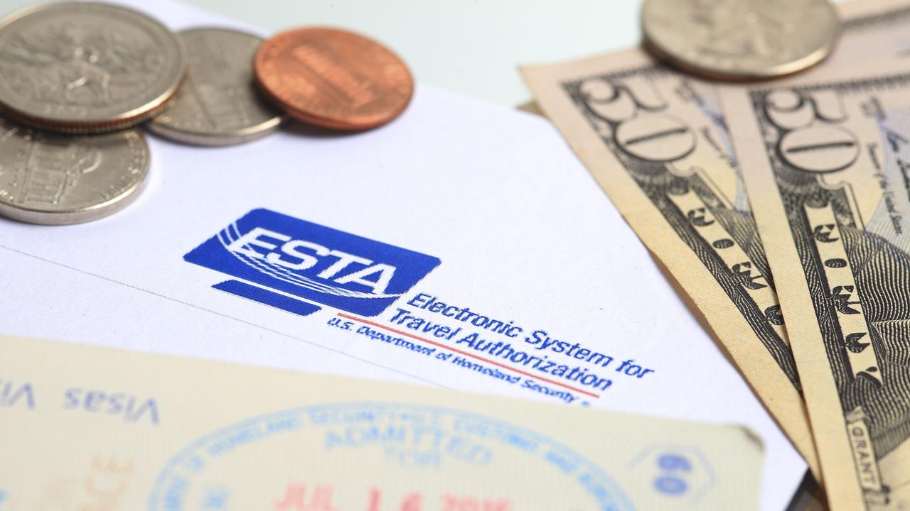 Zusehen sind ein Formular mit der Aufschrift "Esta", US-Dollar-Scheine und Münzen und ein Reisepass mit Stempel.