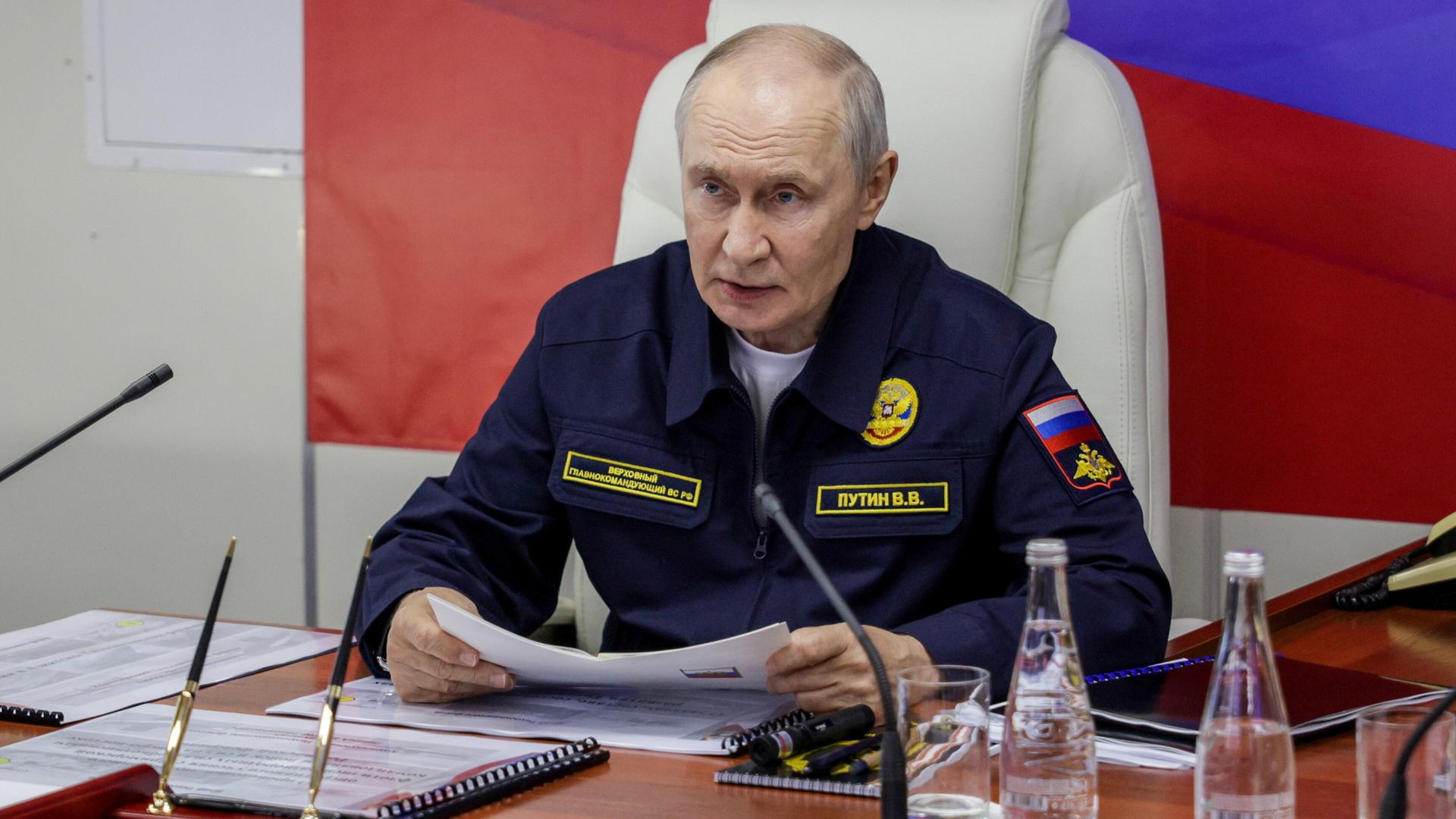 Putin sitzt vor einigen Mikrofonen und hälte ein Dokument in der Hand. Putin sitzt vor einigen Mikrofonen und hälte ein Dokument in der Hand.