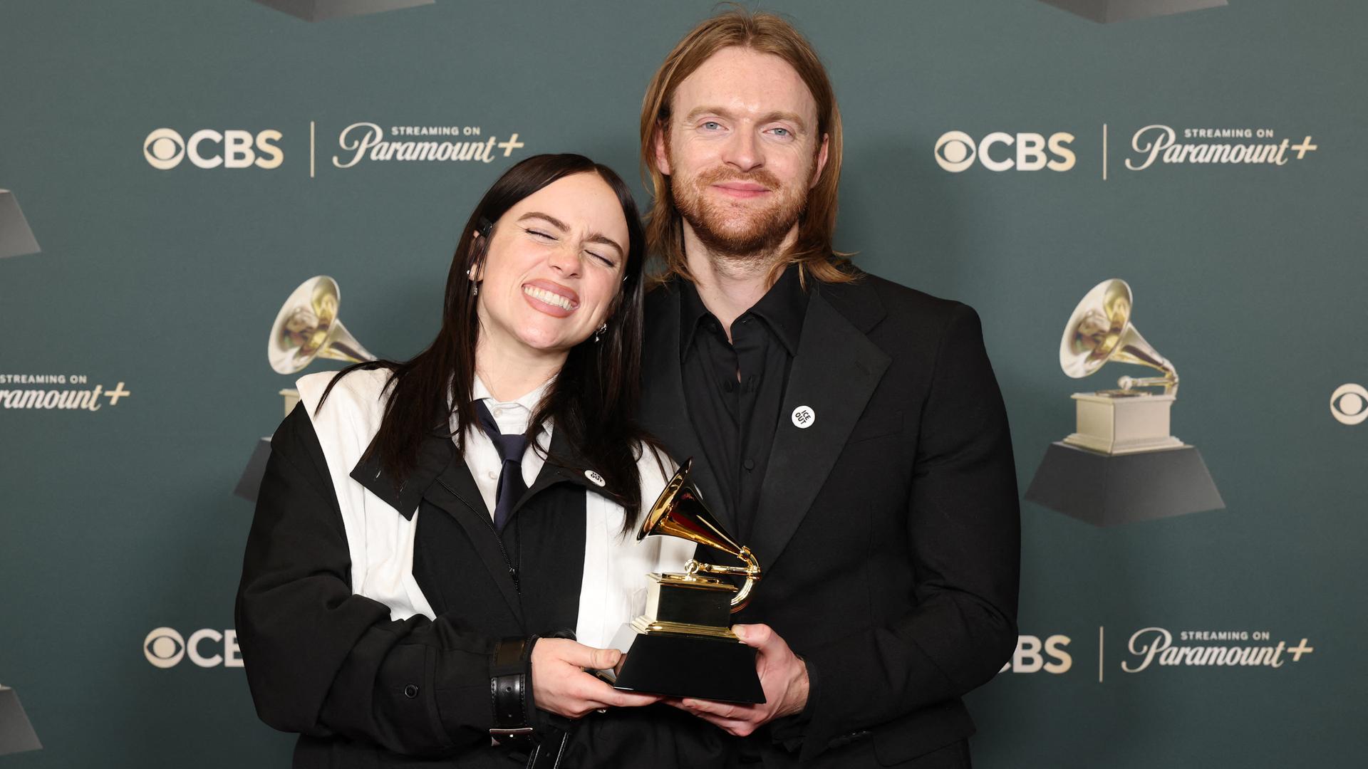 Billie Eilish und ihr Bruder Finneas posieren mit ihrem Grammy vor einer Fotowand. 