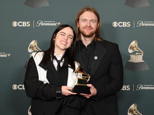 Billie Eilish und ihr Bruder Finneas posieren mit ihrem Grammy vor einer Fotowand. 