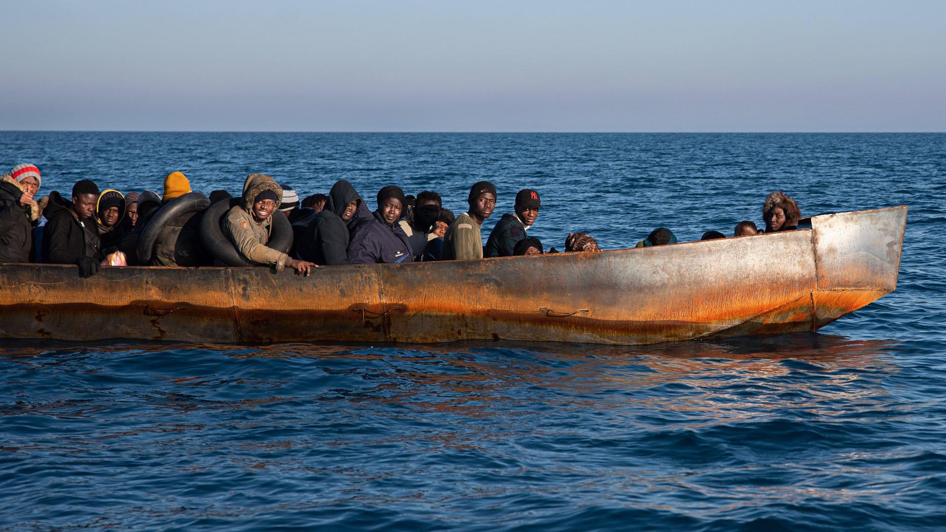 Geflüchtete Personen sitzen dicht gedrängt in einem schwarzen Schlauchboot.