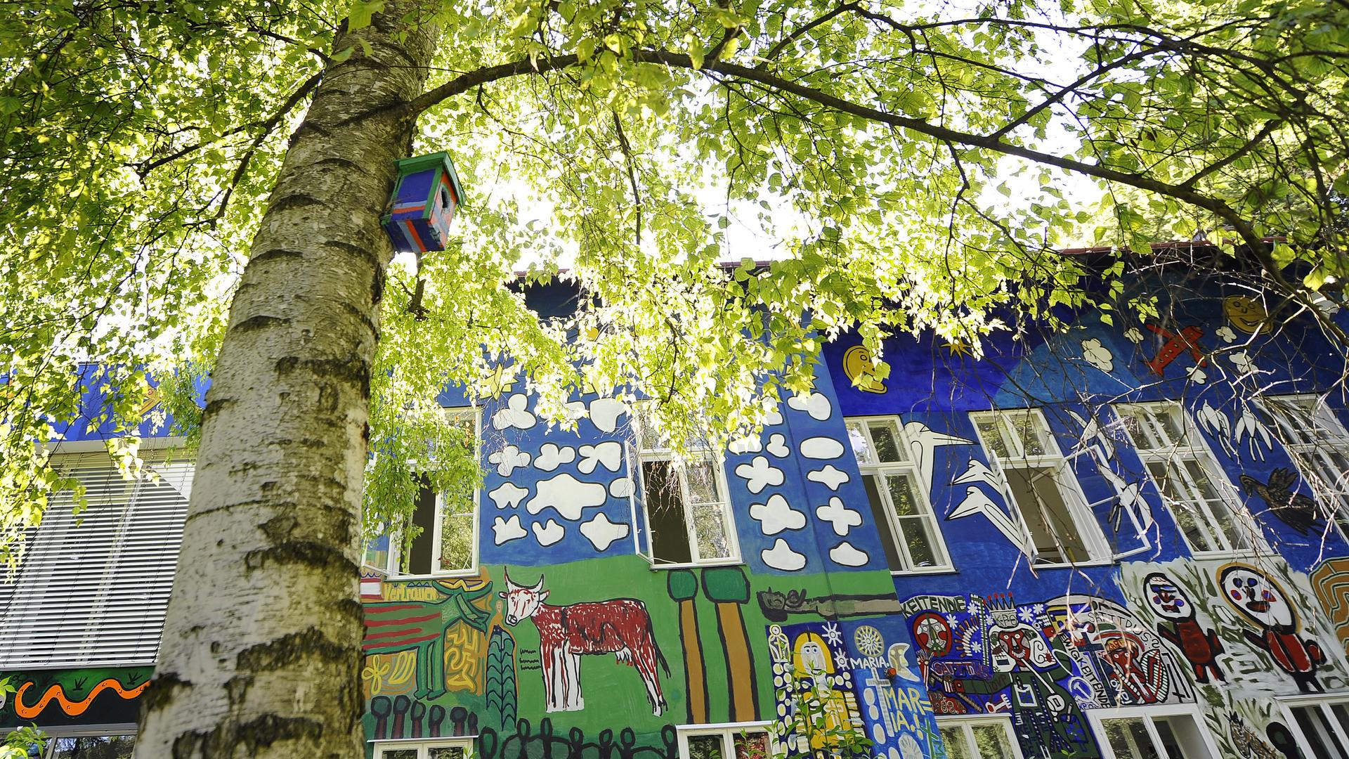 Das Bild zeigt ein mit Art Brut bemaltes Haus, das idyllisch im Wald liegt. Das Bild zeigt ein mit Art Brut bemaltes Haus, das idyllisch im Wald liegt.