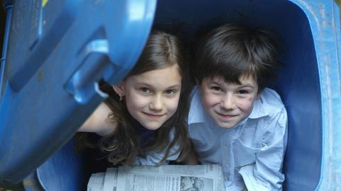 Kinder spielen in Papiermüll-Tonnen
