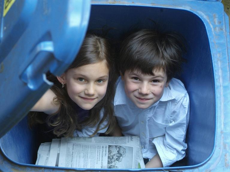 Kinder spielen in Papiermüll-Tonnen