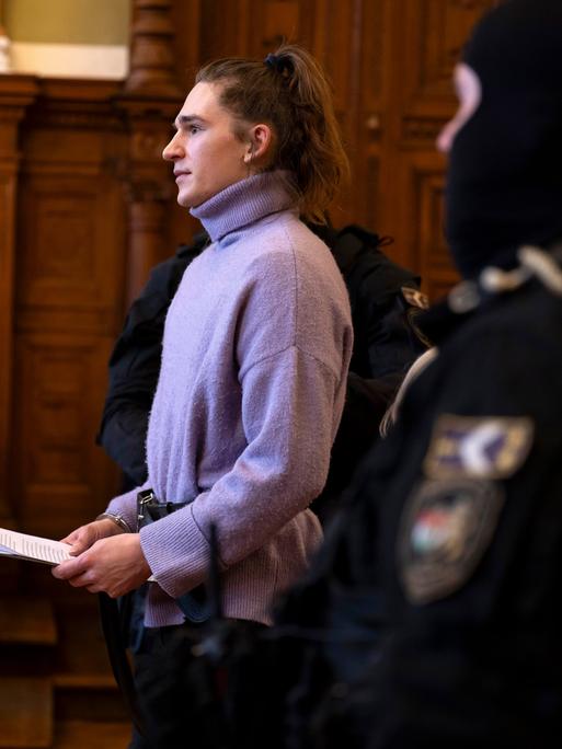 Maja T. trägt einen lila Rollkragenpullover und Handschellen im Gerichtsaal