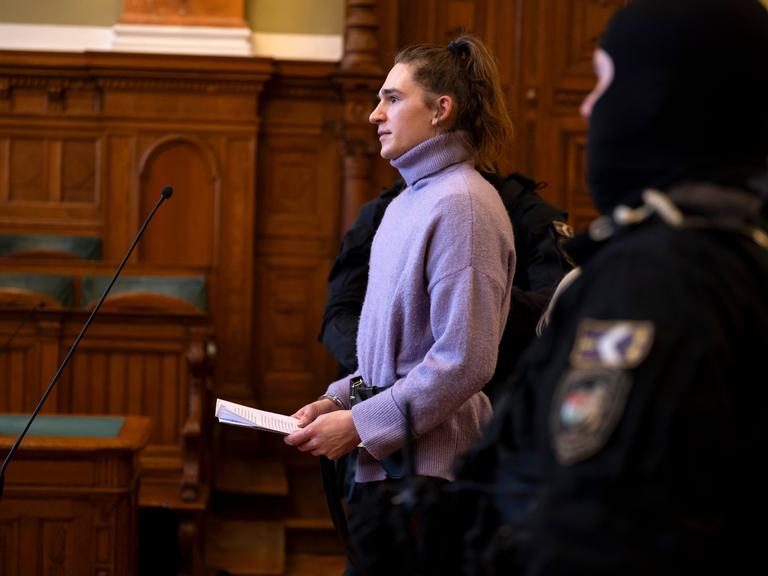 Maja T. trägt einen lila Rollkragenpullover und Handschellen im Gerichtsaal