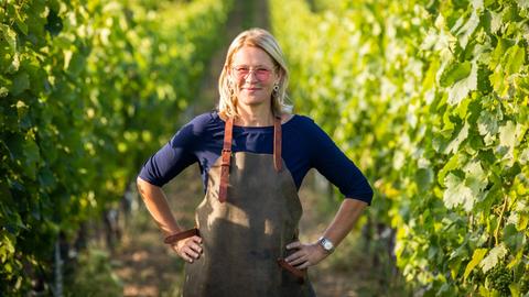 Dorli Muhr steht zwischen Weinreben. Die Hände in die Hüften gestemmt, über der Kleidung eine Schürze. Dorli Muhr steht zwischen Weinreben. Die Hände in die Hüften gestemmt, über der Kleidung eine Schürze.