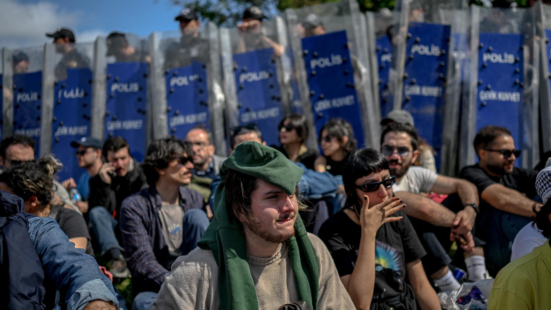 Demonstranten sitzen auf dem Boden, im Hintergrund stehen Polizisten