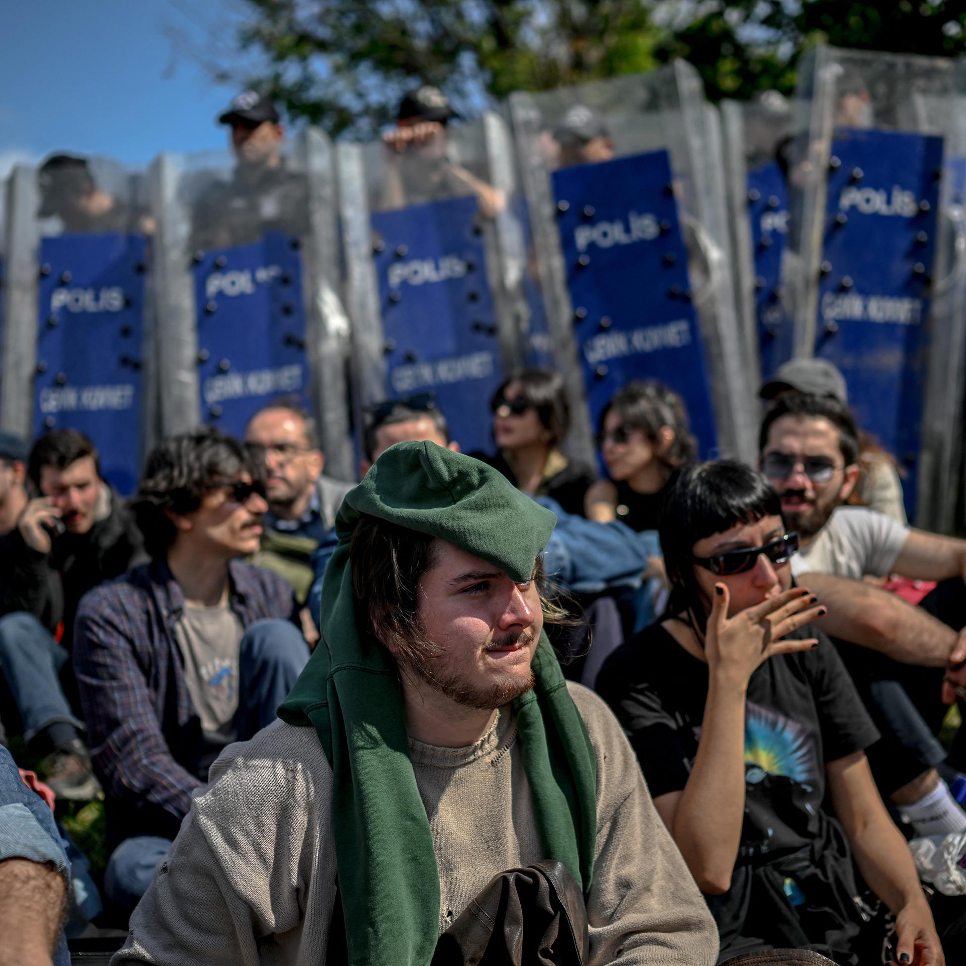 Demonstranten sitzen auf dem Boden, im Hintergrund stehen Polizisten