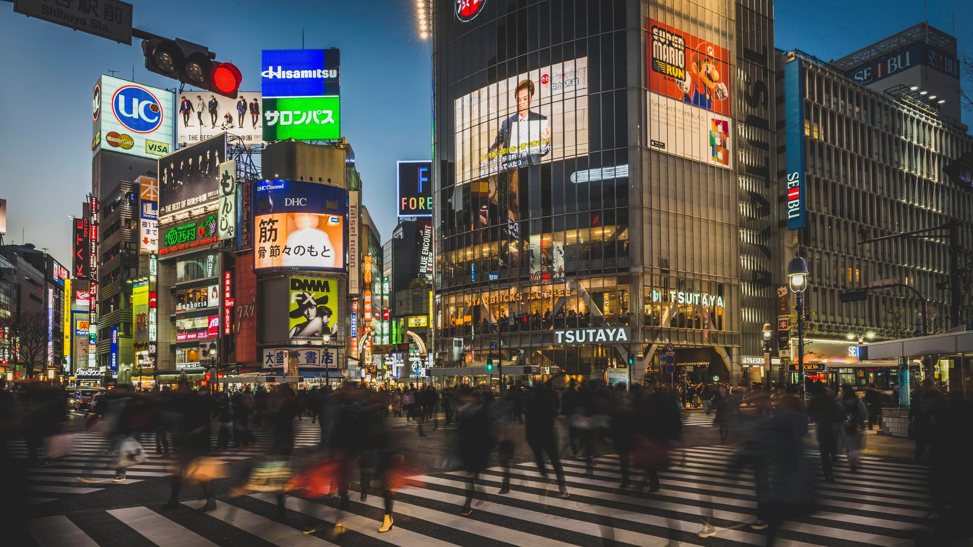 In Tokio überqueren viele Menschen eine Kreuzung, ihre Körper sind Silhouetten.