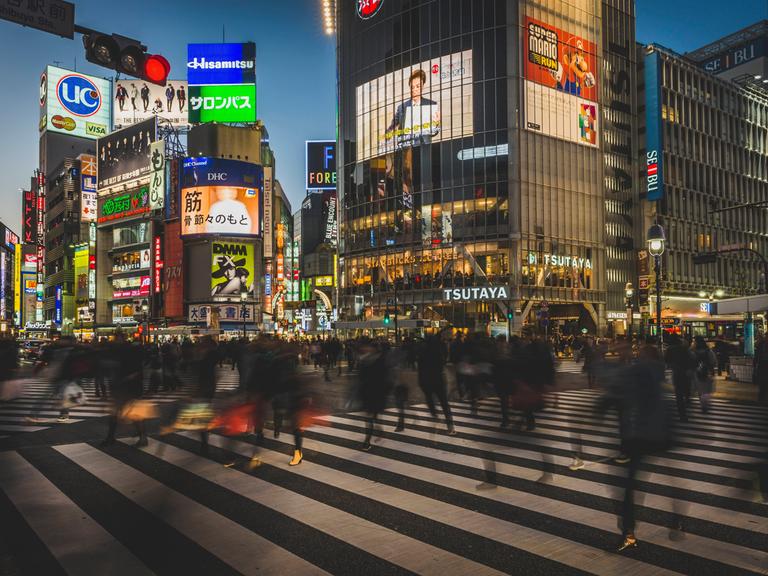 In Tokio überqueren viele Menschen eine Kreuzung, ihre Körper sind Silhouetten.