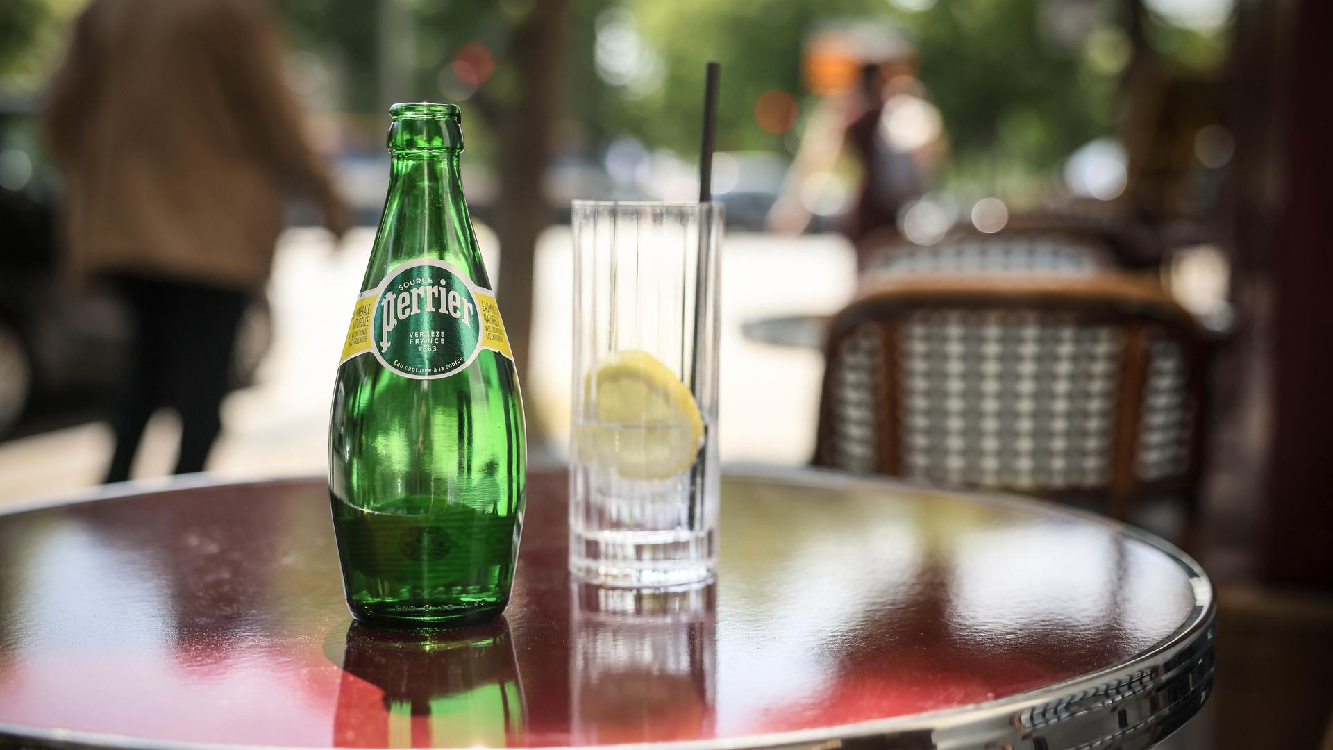 Eine Flasche Perrier steht auf einem Cafétisch, daneben ein Glas mit einer Scheibe Zitrone..
