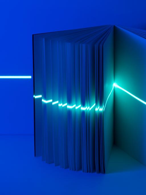 Ein leeres Buch steht in blauem Licht und wird von einem Laser horizontal gescannt.