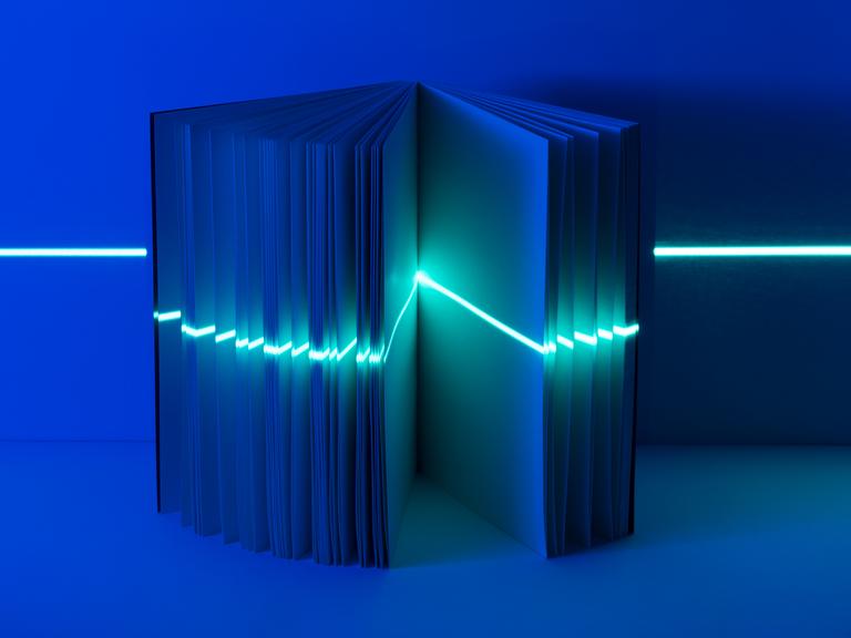 Ein leeres Buch steht in blauem Licht und wird von einem Laser horizontal gescannt.