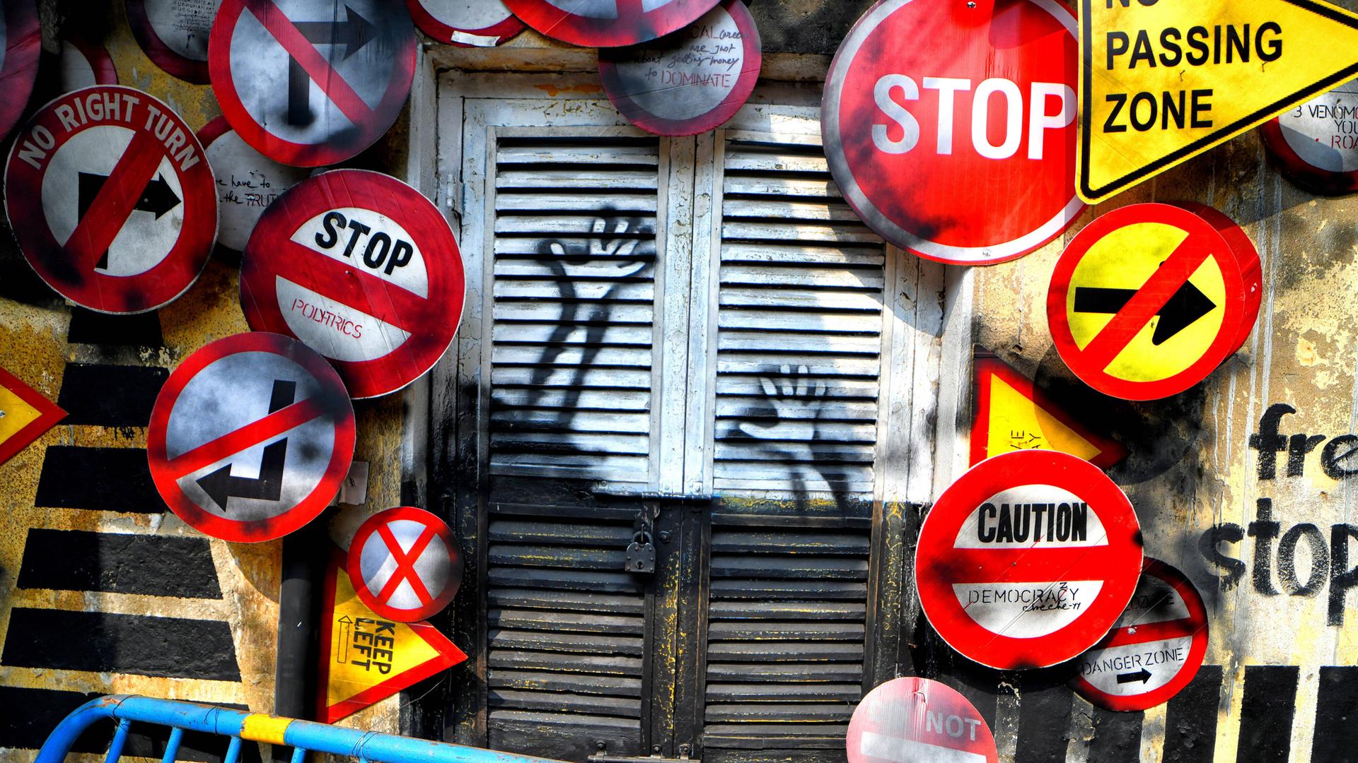  Verschiedene Verkehrsschilder umrahmen einen geschlossenen Rollladen mit Graffiti in Kolkata während des Behala Art Fest im Februar 2022.