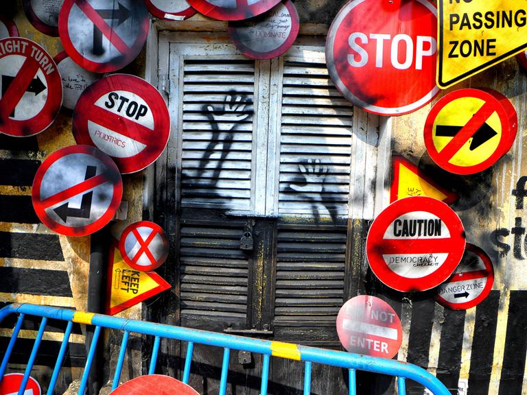  Verschiedene Verkehrsschilder umrahmen einen geschlossenen Rollladen mit Graffiti in Kolkata während des Behala Art Fest im Februar 2022.