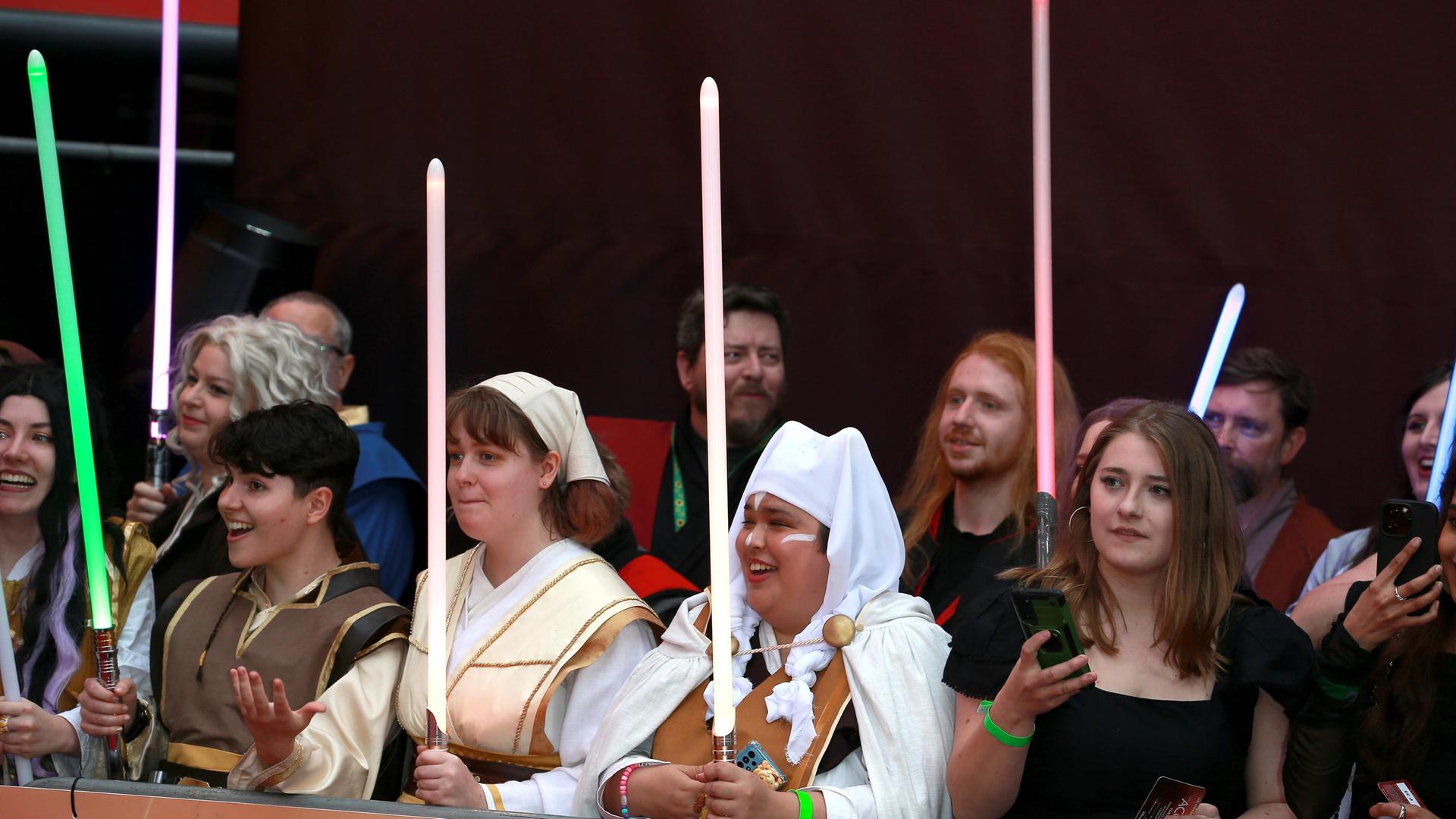 Mehrere weibliche Star-Wars-Fans halten auf der Premiere von Star Wars: Acolyte" Lichtschwerter in die Höhe.