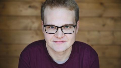 Ein junger Mann mit schwarzer Brille und dunklem T-Shirt
