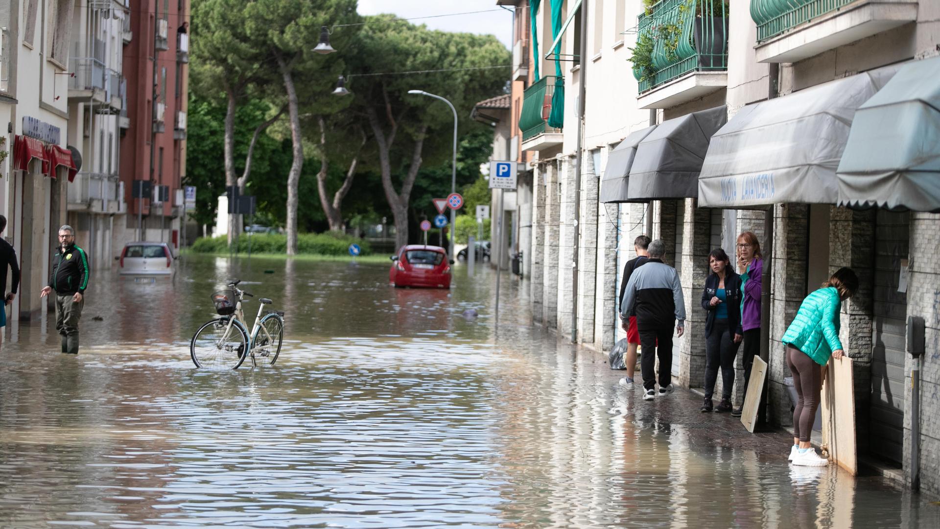 Übeschwemmte Straße, ein Fahrrad steht in der Mitte, links und rechts räumen Menschen auf