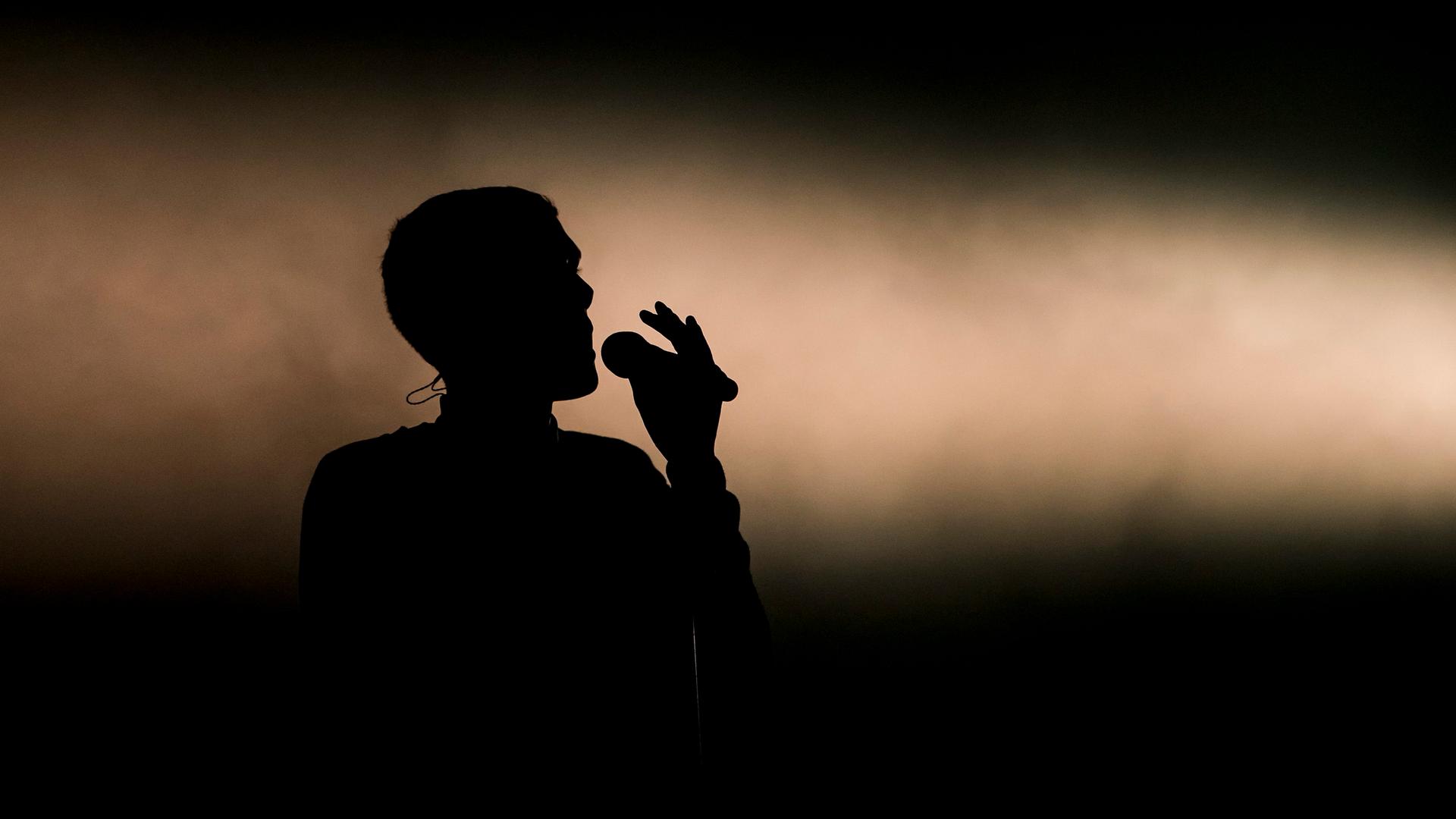 Die Silhouette von Stromaes Kopf, der auf einer Bühne singt.