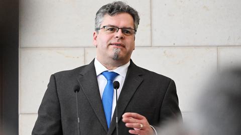Jens Rommel, neuer Generalbundesanwalt, spricht in Mikrofone. Er trägt einen schwarzen Anzug und eine blaue Krawatte. 