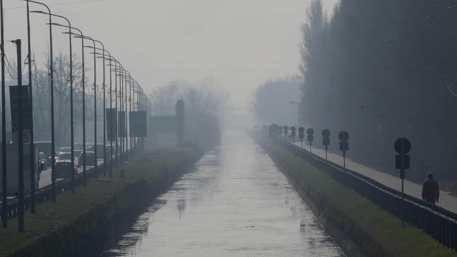 Luft-Verschmutzung in Mailand: Ein Mann geht an einem Kanal entang, es ist grau und nebelig. 