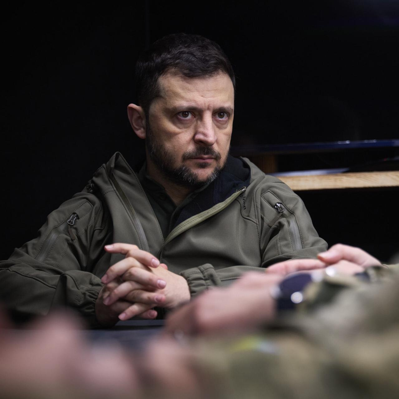 Präsident Wolodymyr Selenskyj sitzt ernst blickend im Armeeparka an einem Schreibtisch